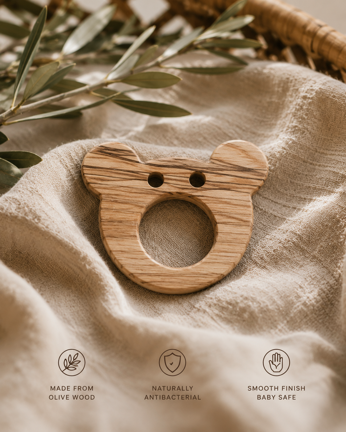 Wooden bear-shaped teething ring on a textured fabric background with olive leaves.