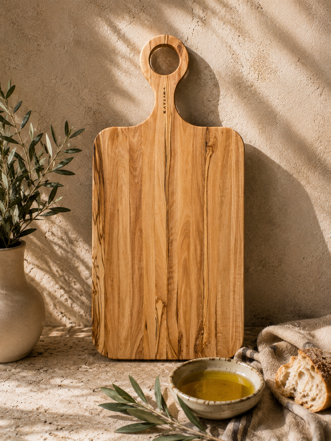 Wooden cutting board with a handle on a rustic surface with a plant and bread.