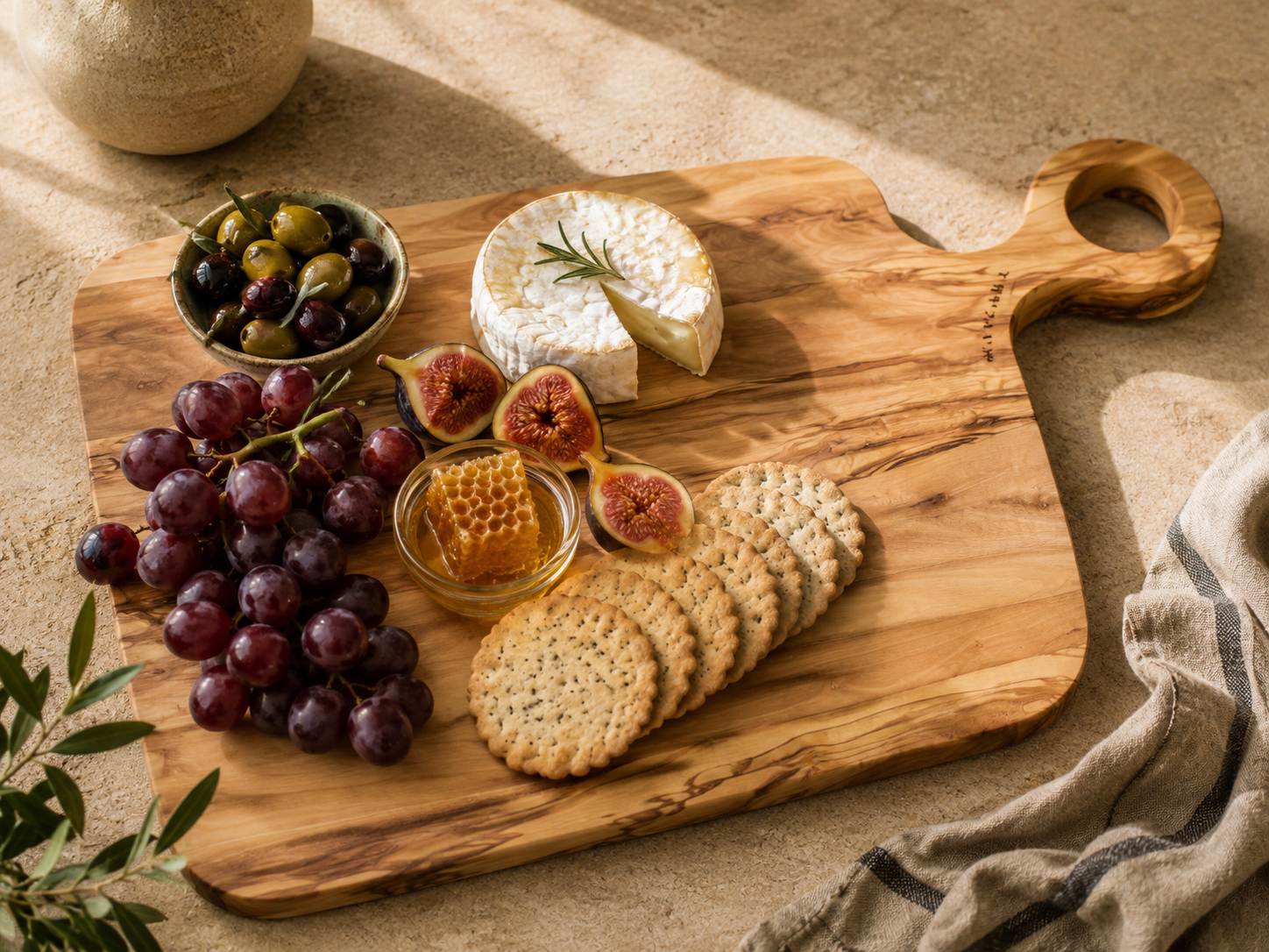 Wooden cutting board with cheese, grapes, figs, and crackers on a textured surface.
