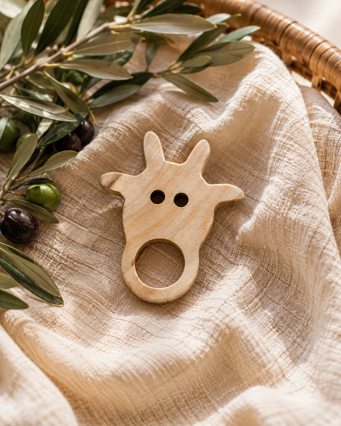 Wooden cow-shaped teether on a textured fabric surface with green leaves in the background