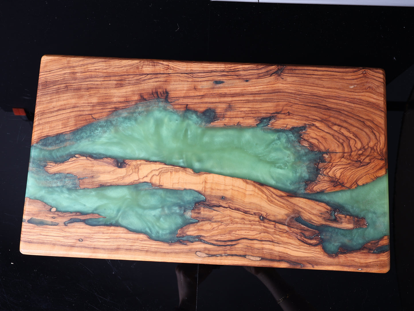 Wooden cutting board with green resin inlay on a black background
