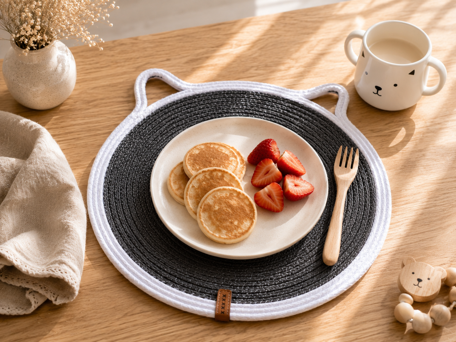 Plate of pancakes with strawberries on a woven placemat on a wooden table.