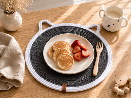 Plate of pancakes with strawberries on a woven placemat on a wooden table.