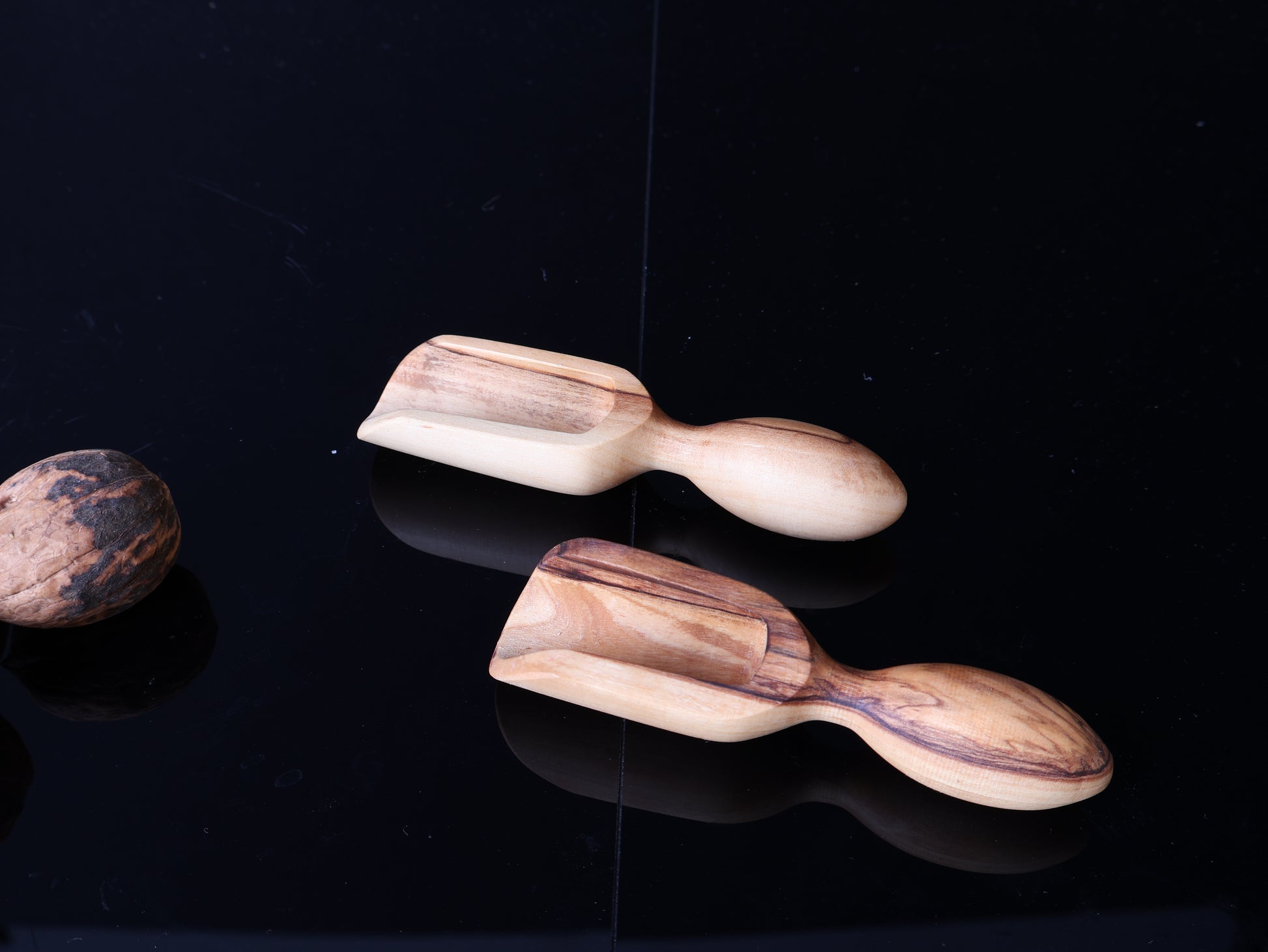 Two wooden tea infusers on a black reflective surface