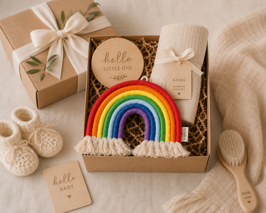 Baby gift set with rainbow toy, booties, and other items in a box on a soft surface.