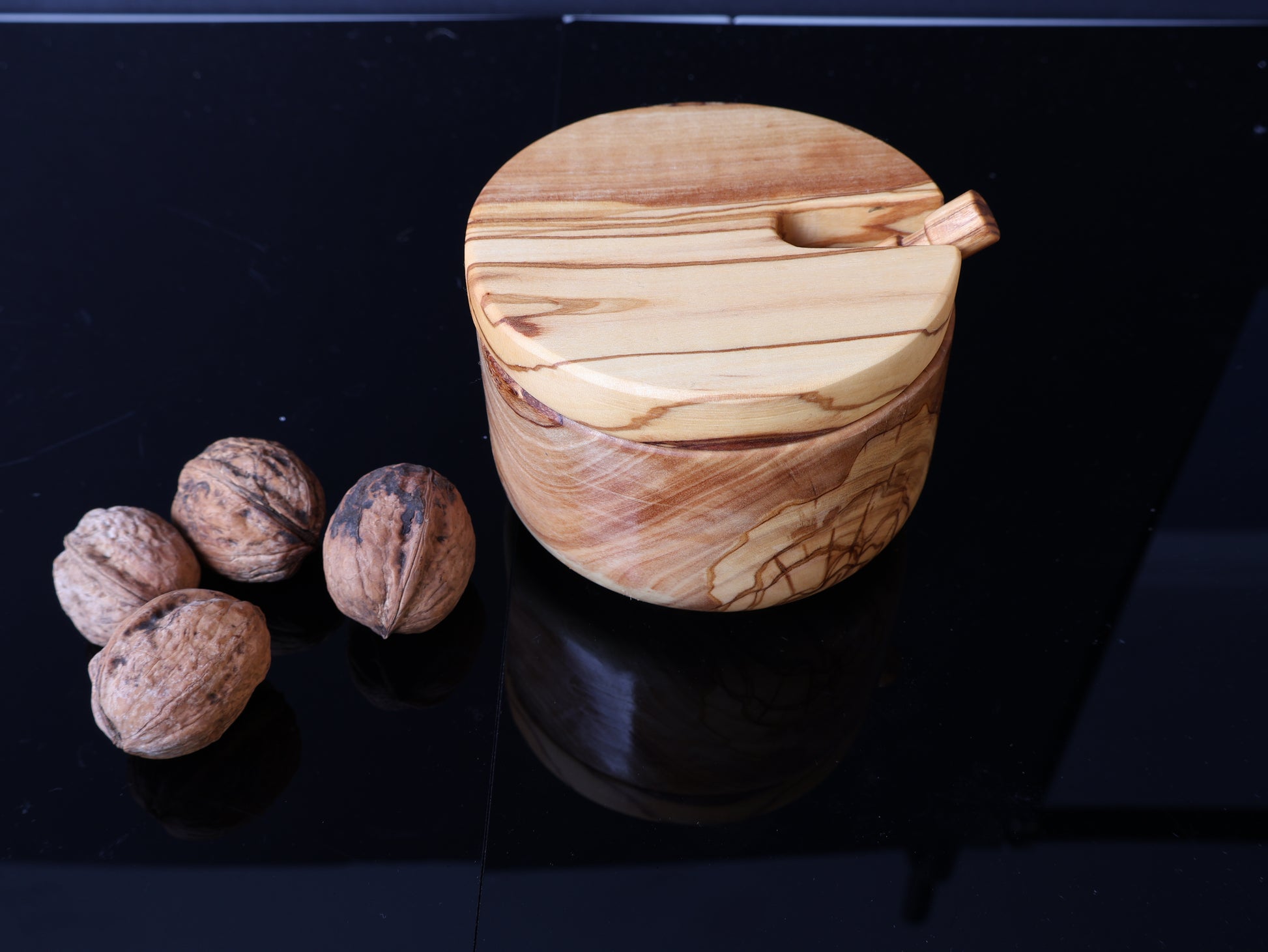 Wooden container with lid next to walnuts on a dark surface