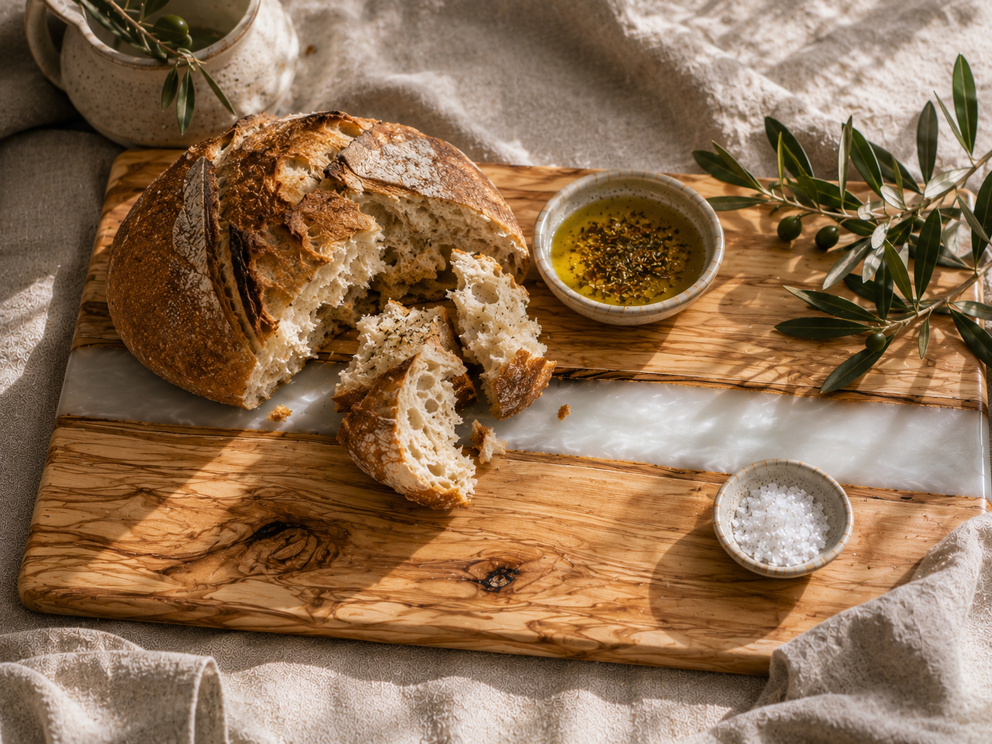 Loaf of bread on a wooden cutting board with olive oil and salt, on a textured fabric background.